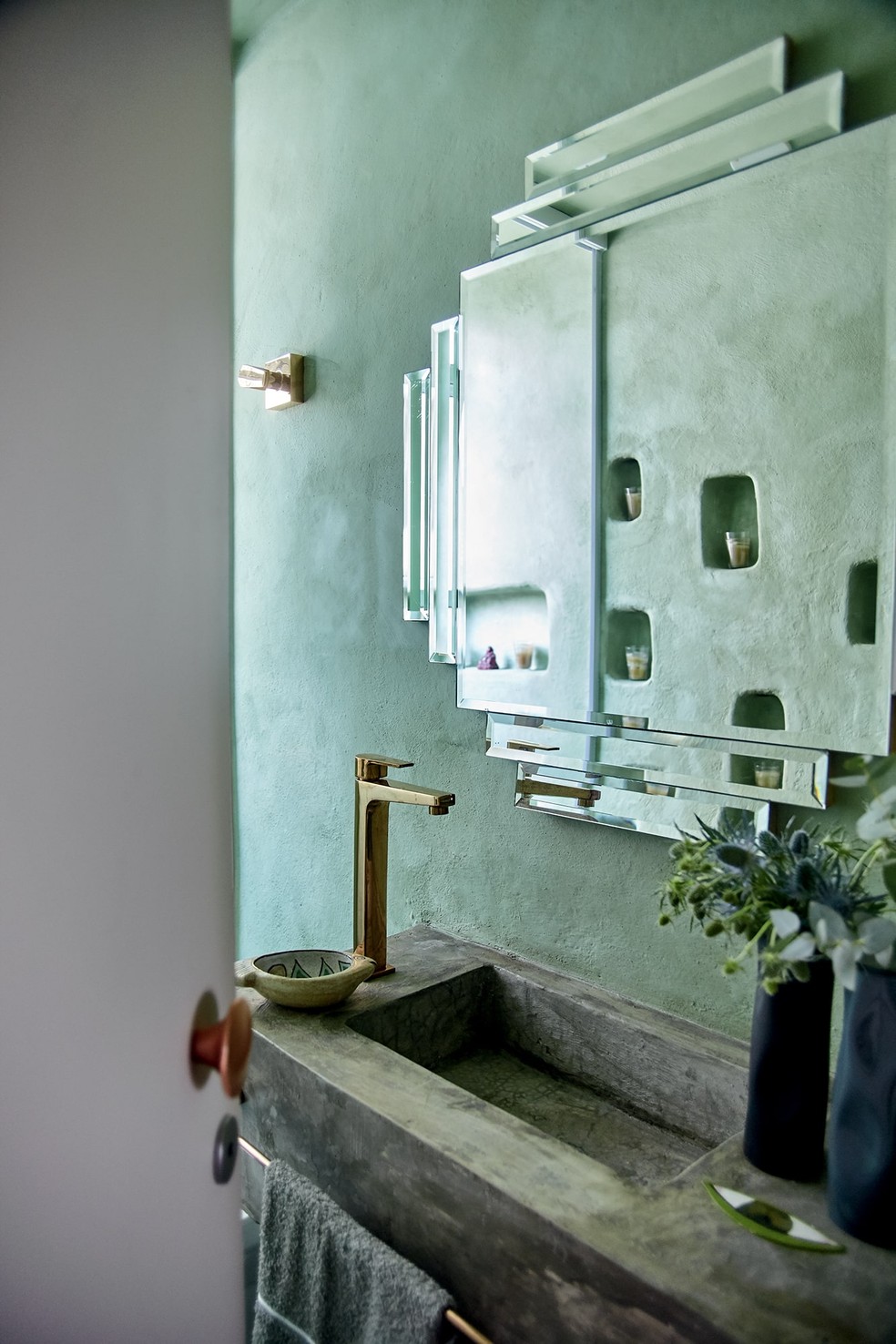 Lavabo exibe nichos na parede escavados manualmente para abrigar velas, refletidos no espelho art déco, presente do filho, Lucca — Foto: Ilana Bessler/Habitado Projeto