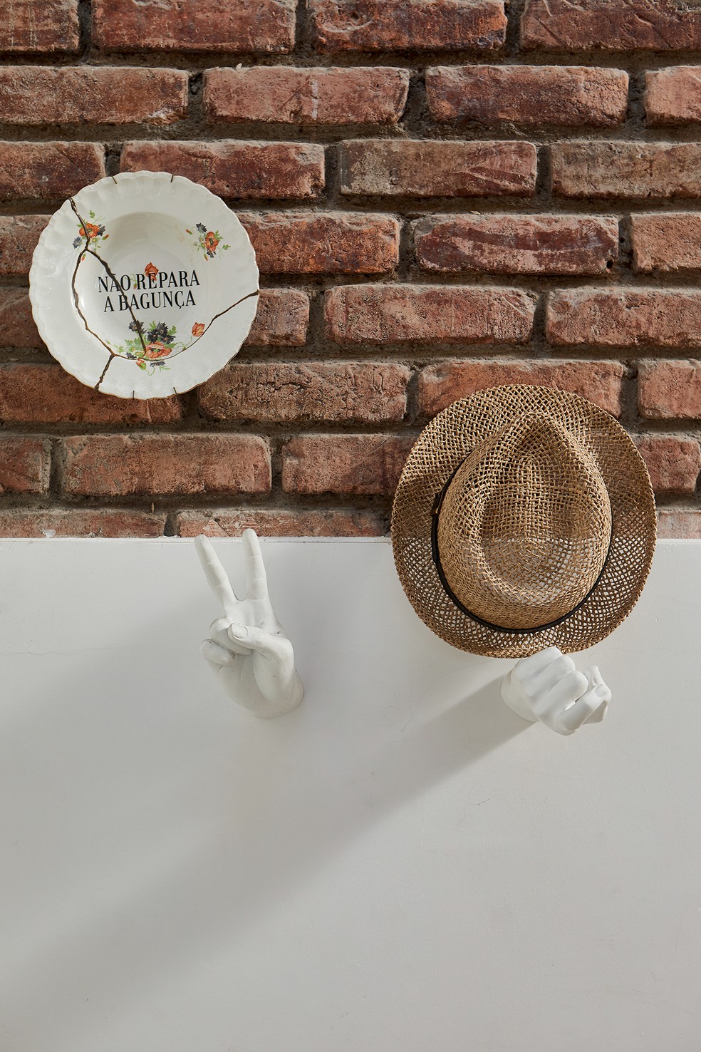 Detalhe da parede da sala decorada com prato da loja Lou, esculturas em formato de mão garimpadas pelo casal e chapéu de palha comprado na Itália — Foto: Deco Cury