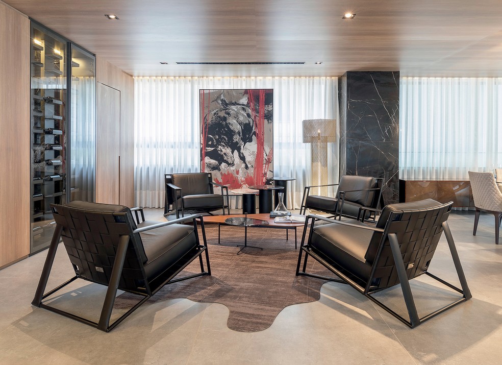 Para o lounge da adega, o arquiteto selecionou poltronas e luminária de piso da Tonino Lamborghini e desenhou um tapete de formato orgânico exclusivamente para o projeto, executado pela Tapetah — Foto: Raphael Briest