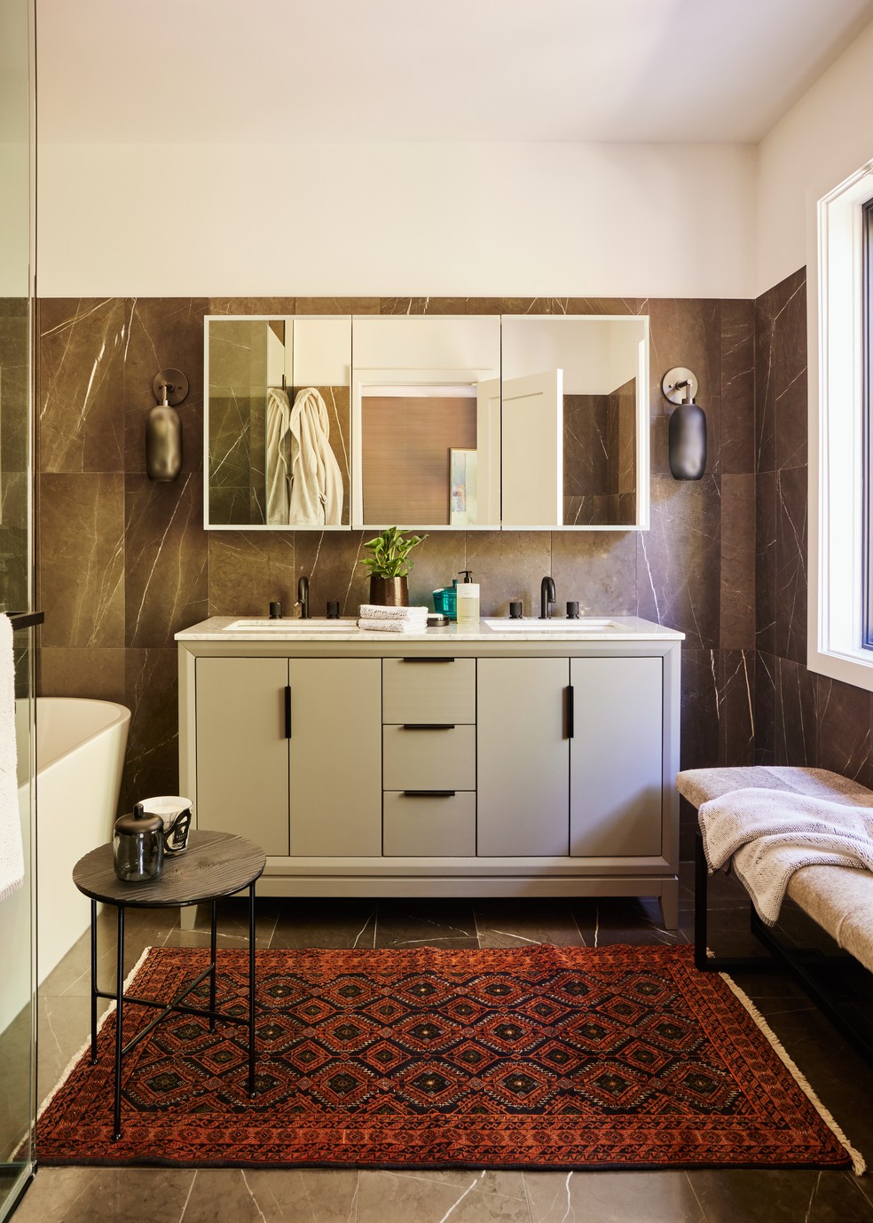 Banheiro traz azulejos na cor marrom, tapete estampado e armários na cor branca — Foto: Marc Oliver Becotte