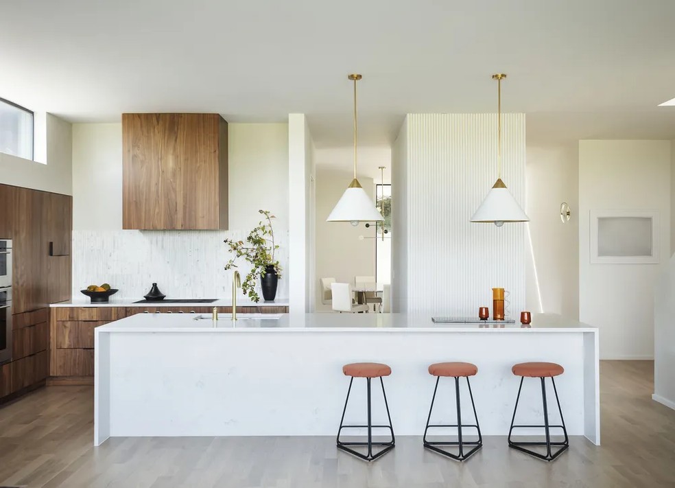 A cozinha branca traz toques de cores nos armários revestidos com madeira e nas banquetas. O projeto é da designer de interiores Sara Cukerbaum — Foto: Matthew Williams