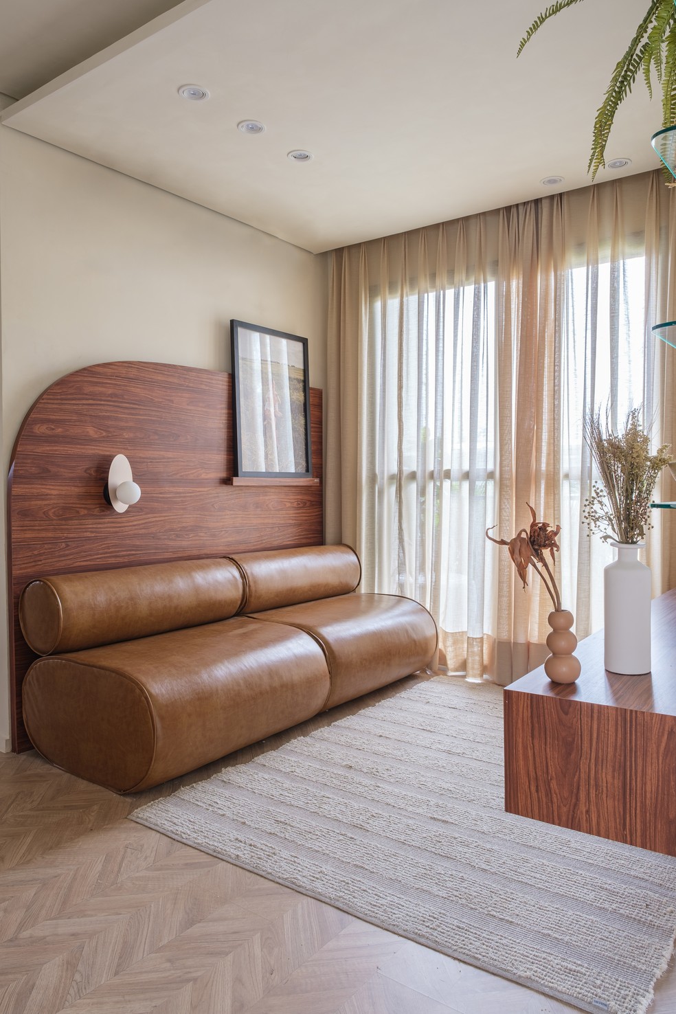 Na área de estar, Larissa optou por um sofá de couro com formatos arredondados - no piso, um laminado de madeira com padronagem espinha de peixe ajuda a elevar a sofisticação do projeto — Foto:  Raphael Medeiros