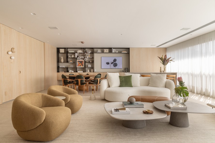 A integração entre living, sala de jantar e área gourmet é total: o que parece apenas um painel de madeira ao fundo é, na verdade, uma porta de correr que revela uma bancada com churrasqueira