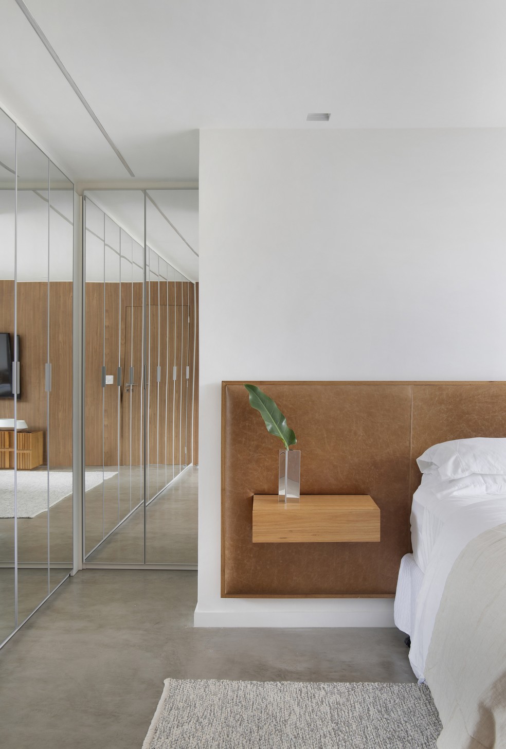Materiais naturais compõem o projeto de décor. No quarto principal, a cabeceira da cama é revestida de couro — Foto: Anita Soares