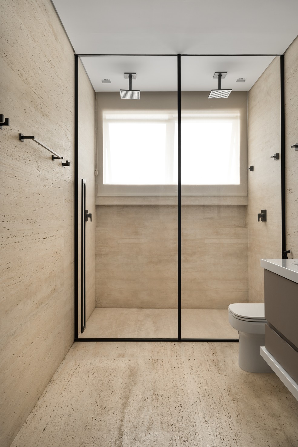 Coberto de mármore travertino, o banheiro do casal é neutro e sofisticado — Foto: Estúdio NY18