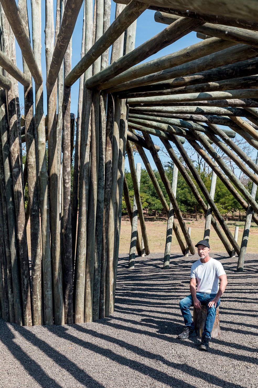 Humberto Campana posa sob as toras que formam o pavilhão de eucalipto, uma das seis instalações de arte ao ar livre que já estão prontas para a abertura do Parque Campana no ano que vem – quando estiver completo, o local vai abrigar 12 pavilhões ao todo — Foto: Filippo Bamberghi