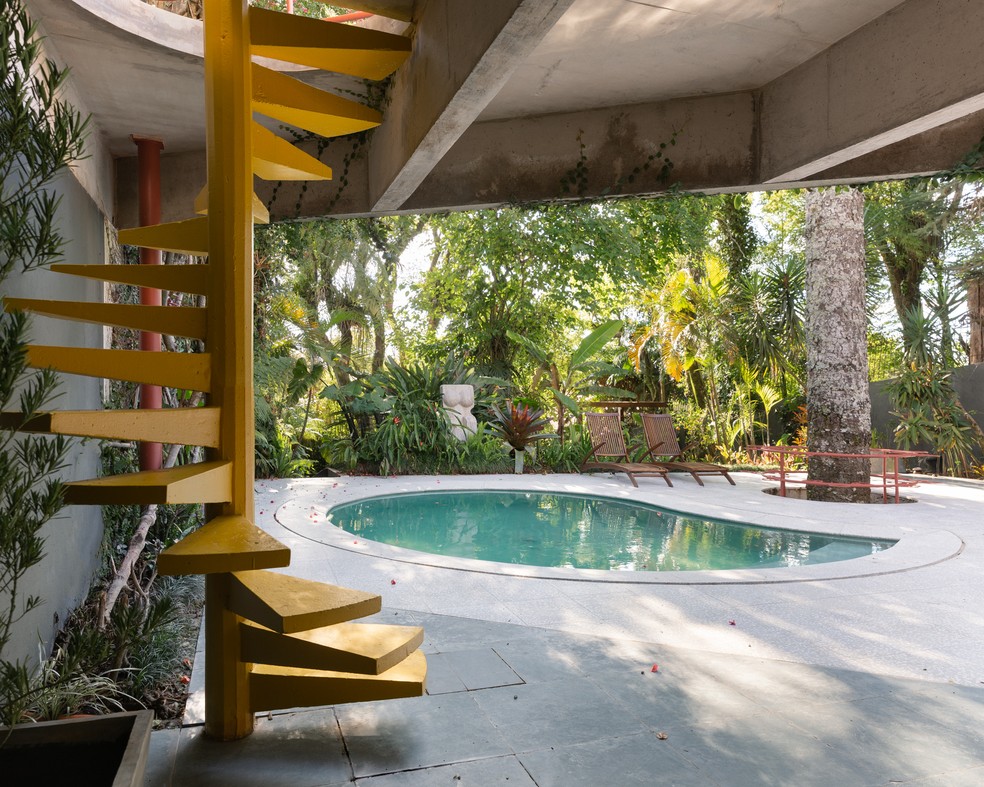 Ao fundo do terreno, um desnível e uma escada em caracol desembarca na área da piscina, com formato orgânico, típico da década de 1970 — Foto: Brenda Pontes