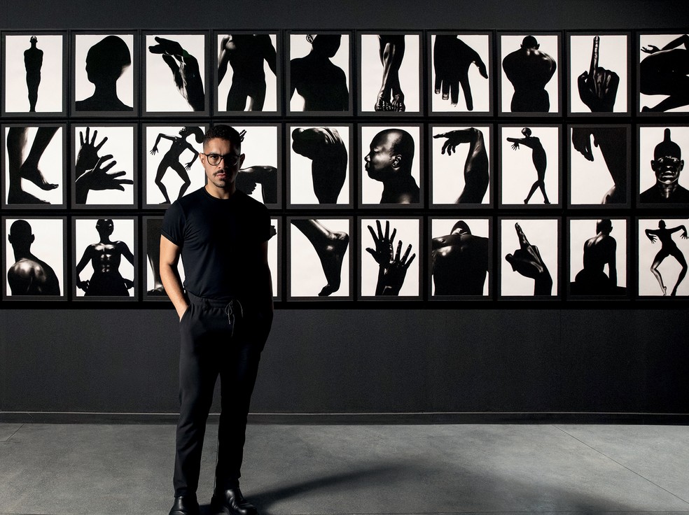 Gustavo Nazareno posa em frente à coreografia composta pela série de desenhos em carvão sobre papel Bará (2019-2023) — Foto: Deco Cury