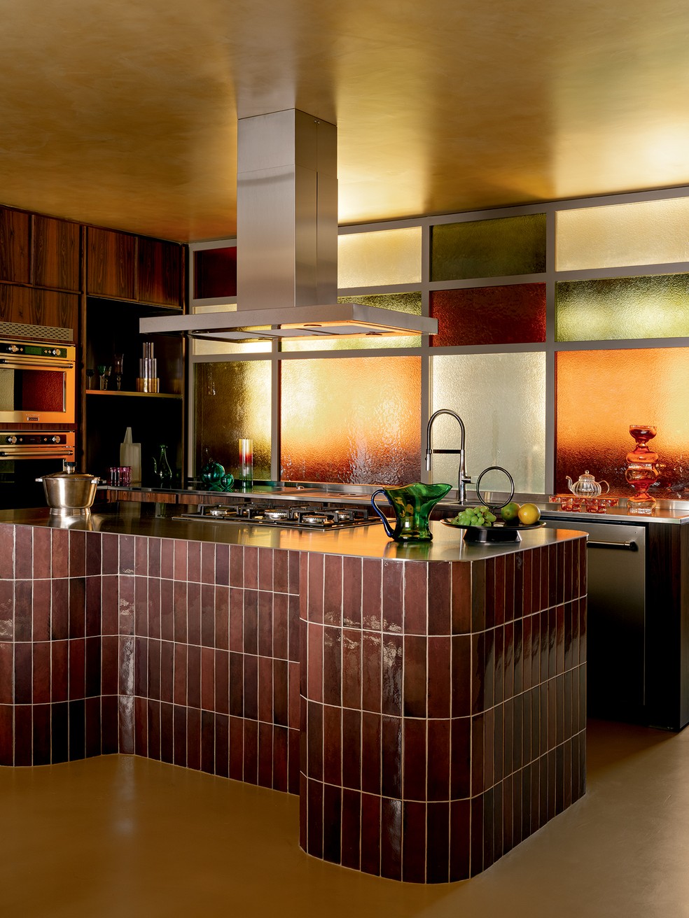 A cozinha exibe marcenaria da ID Móveis, bancadas de aço inoxidável da Artsteel, com bandeja Espelho d’Água e vaso Respiro, do F. Studio, na Dpot Objeto (ao fundo, à dir.), ilha revestida de porcelanato da Portobello, com balde de gelo vintage, na Casa Operandi, e bandeja da coleção Stacks, design Brunno Jahara para a St. James, na Dpot Objeto (da esq. para a dir.), e eletrodomésticos da Brastemp — Foto: Fran Parente | Estilo: Adriana Frattini | Produção: Bruna Scapim