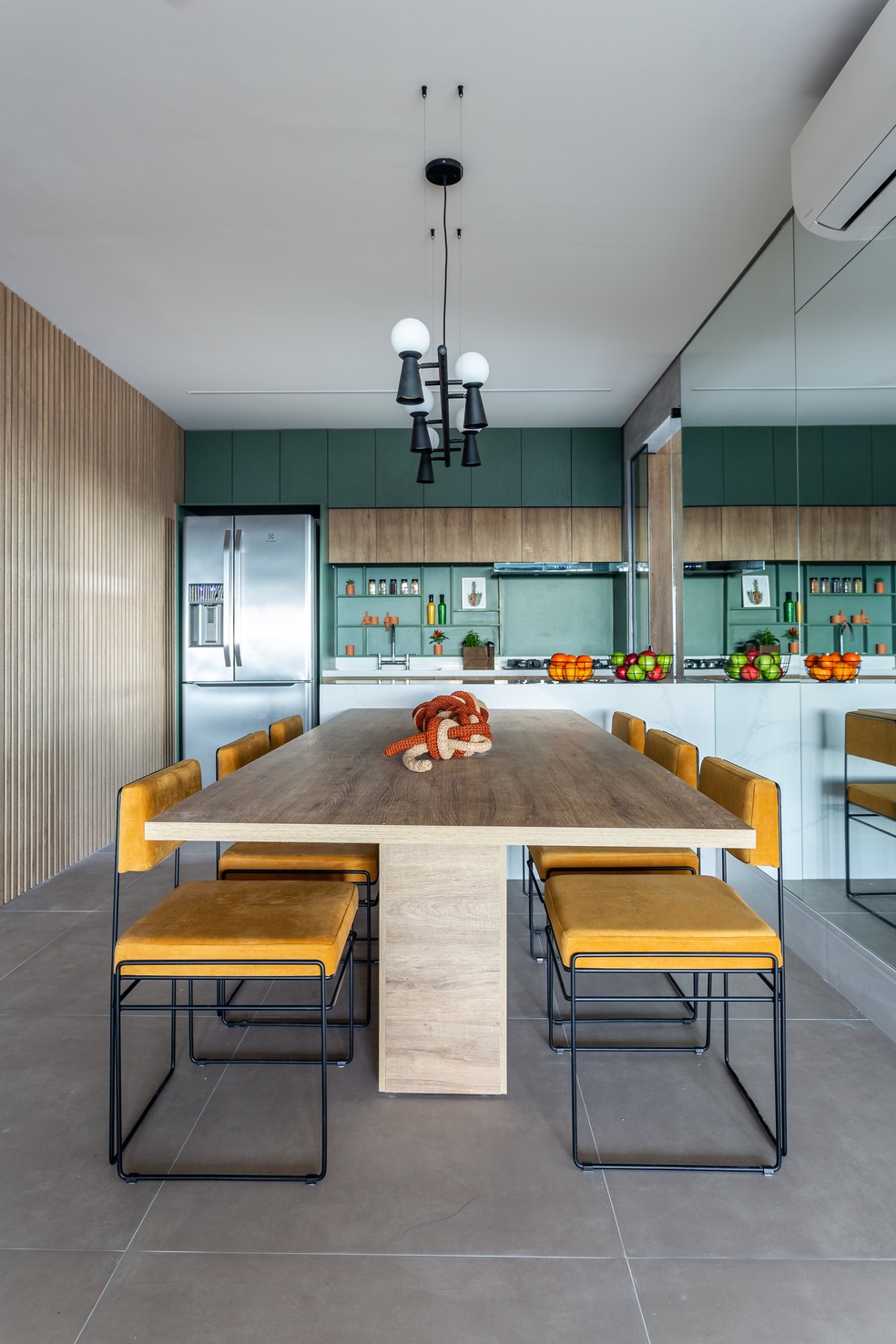 Na sala de jantar, o pendente Pivô 5, de Tadeu Omae, paira sobre a mesa de seis lugares que emoldura a cozinha aberta ao fundo — Foto: Kelly Queiroz