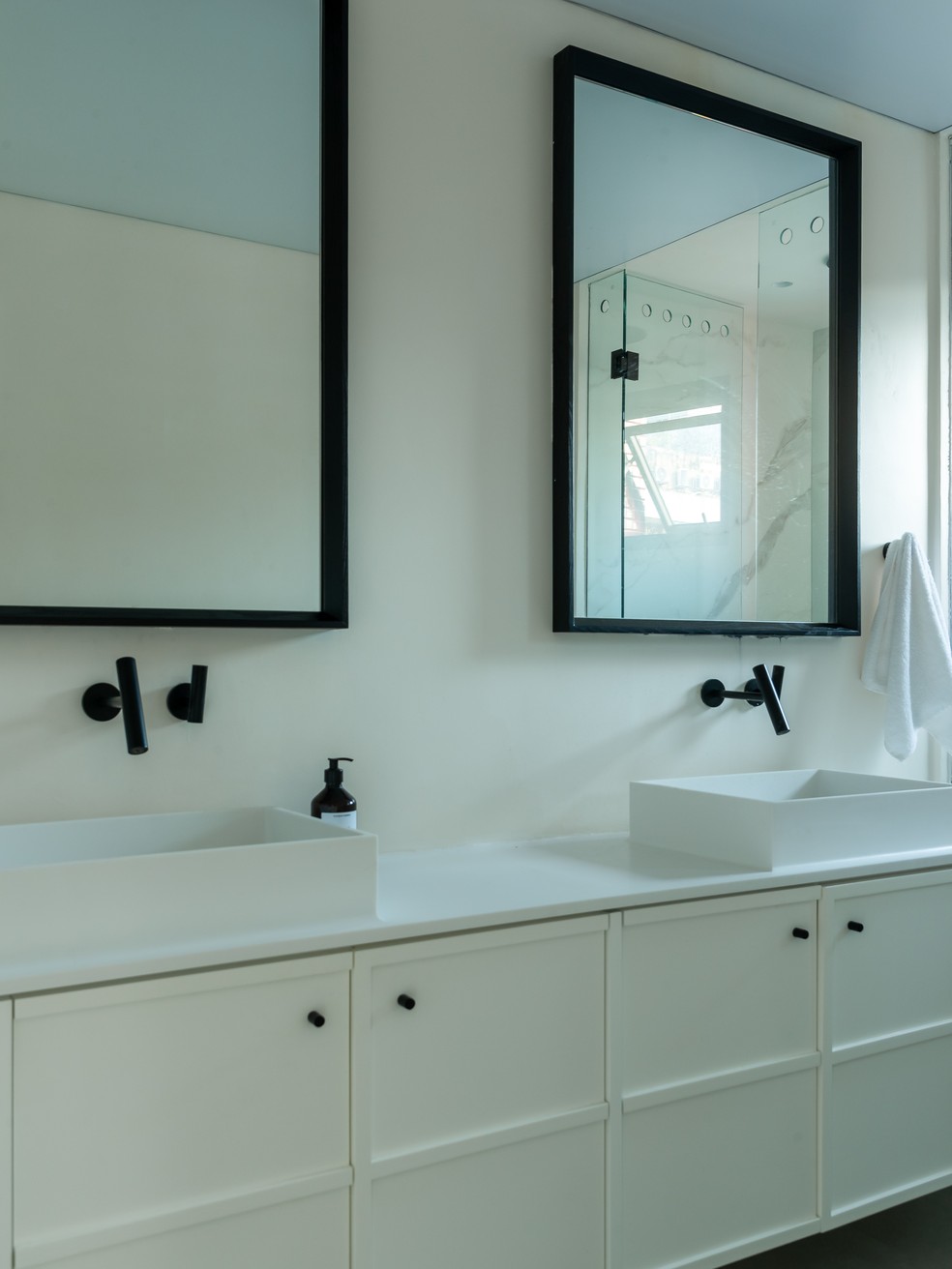No banheiro da suíte, bancada em corian branco sobre armários da Marcenaria Morada, de onde também vêm os espelhos — Foto: Wesley Diego Emes