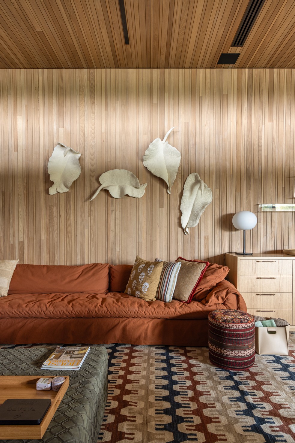 Assinado pela designer Marina Linhares, este ambiente conta com paredes e forro de madeira, obras de arte em cerâmica, sofá em algodão (Entreposto), pufe Botteh em lã e algodão e tapete By Kamy — Foto: Evelyn Müller