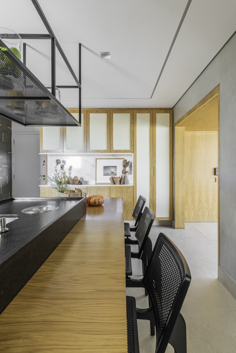 Na cozinha, em primeiro plano, a bancada de refeições de madeira e, ao fundo, o armário exibe portas em palha indiana natural  — Foto: Guilherme Pucci