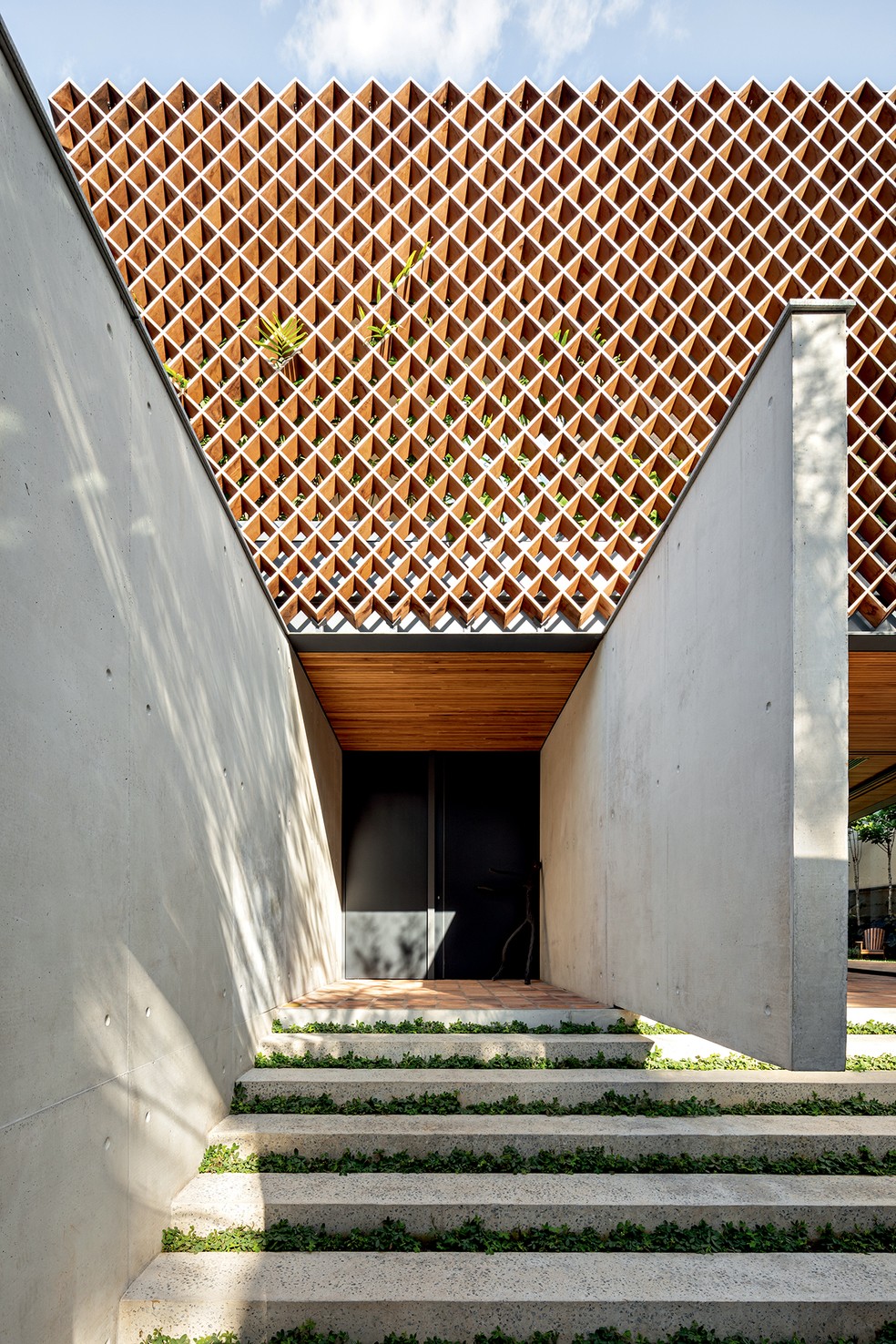 A escadaria de concreto, conectada ao jardim, conduz à entrada da casa, elevada em relação ao nível da rua – a empena possui uma das extremidades em balanço, conferindo leveza à arquitetura — Foto: Fran Parente