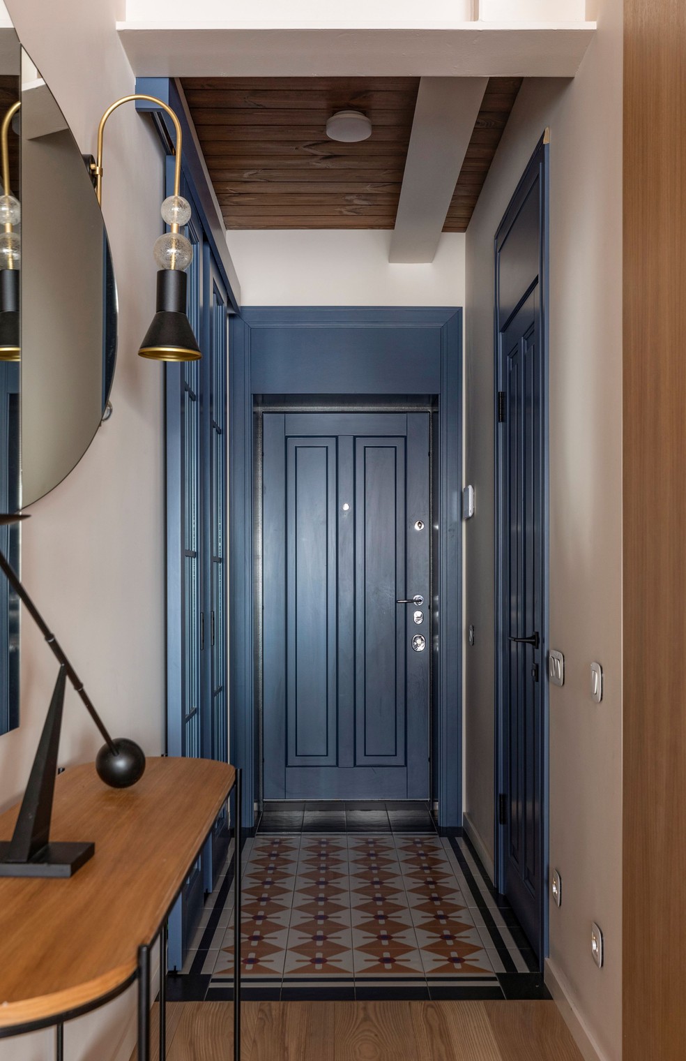 O hall de entrada difere do restante do apartamento ao explorar as estampas do piso de ladrilho hidráulico e o tom fechado de azul das portas — Foto: Yevhenii Avramenko