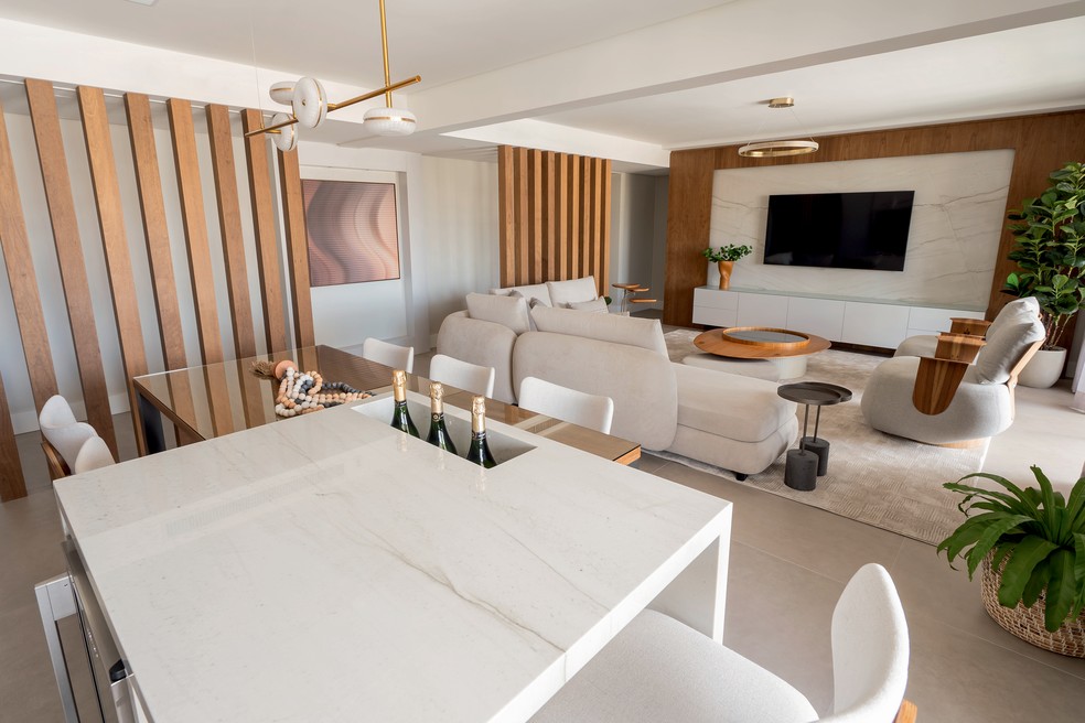 A partir do espaço gourmet é possível ver os dois conjuntos de brises de madeira que demarcam os ambientes no living integrado — Foto: William Rossoni