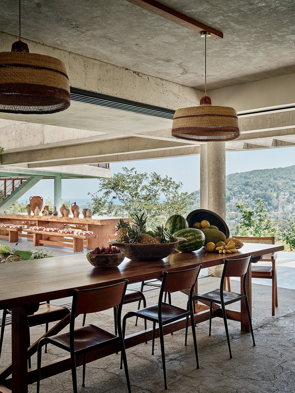 A sala de jantar, abraçada pela natureza, recebeu pendentes tecidos à mão por Sara Efia Reddin, do Golden Studio, sobre mesa com cadeiras escolares francesas vintage, na Mullca — Foto: Frank Frances