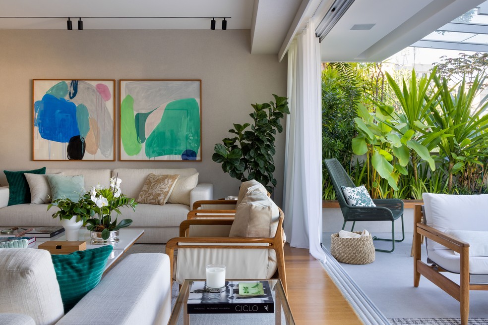 Sala de estar e varanda se conectam por meio de plantas e móveis em cores sóbrias — Foto: André Nazareth