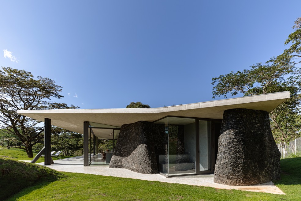 Vista da casa com a estrutura sinuosa revestida de pedras portuguesas pretas — Foto: Luisa Lage