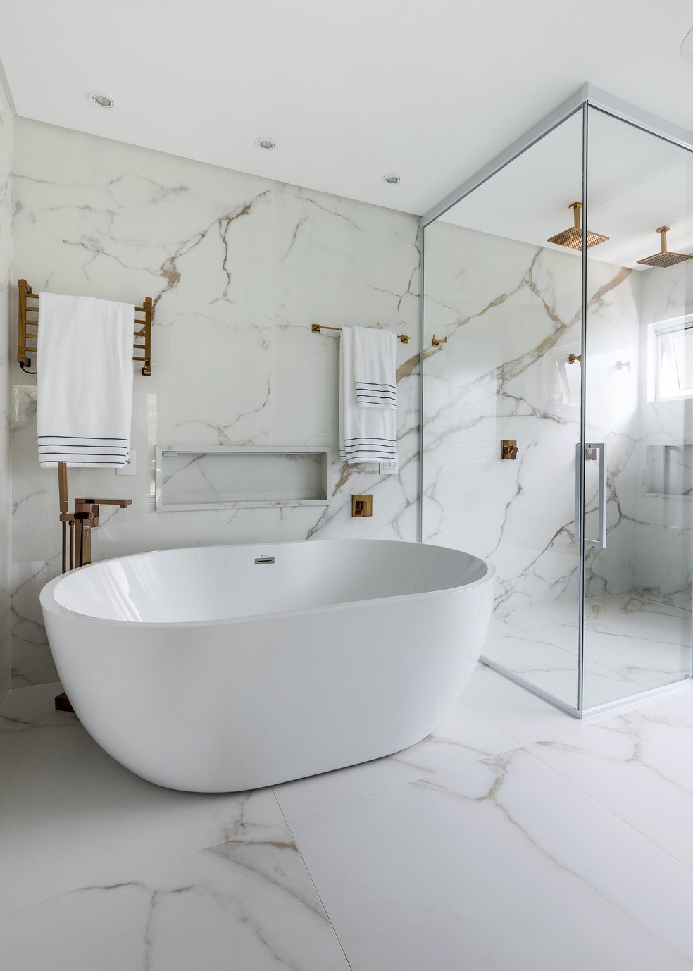Clima de spa no banheiro da suíte master com banheira de imersão, mármore e metais dourados — Foto: Lio Simas
