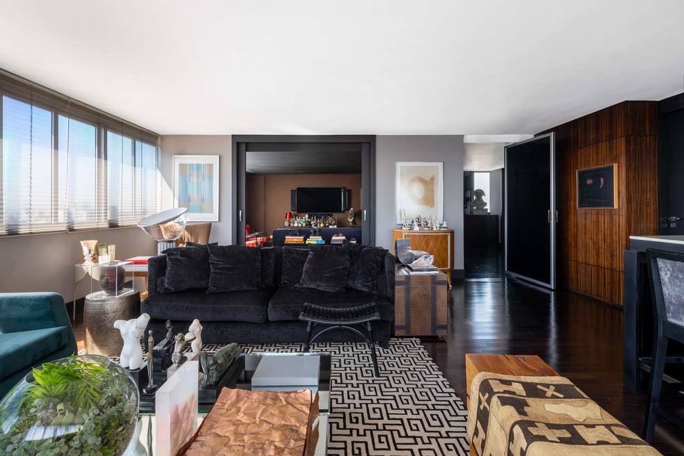 O living é rodeado pelo skyline curitibano. A grande porta preta se abre para o hall de entrada e combina com o piso de imbuia ebanizada da Masterpiso. O tapete geométrico é da By Kamy e, ao fundo, atrás do sofá, destaque para a luminária de mesa Taccia, de Achille and Pier Giacomo Castiglioni — Foto: Bia Nauiack | Produção: Rita Teodorovicz