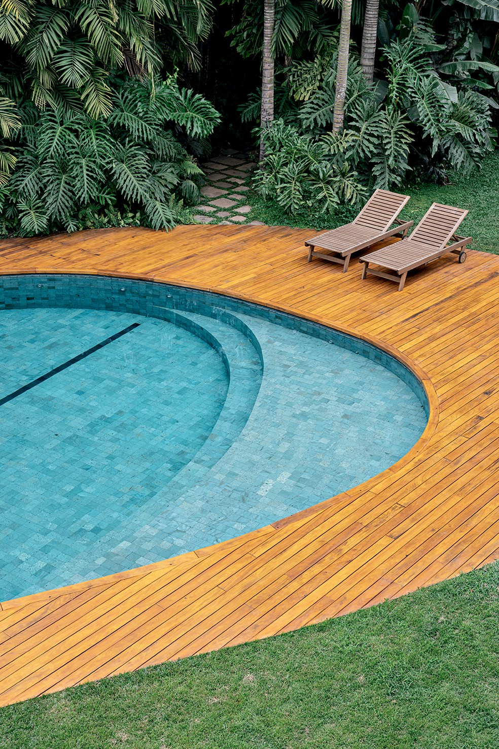 A piscina de formas sinuosas arrematada por um deque de madeira é o ponto alto do jardim, contrabalanceando as linhas retas predominantes na arquitetura — Foto: Fran Parente
