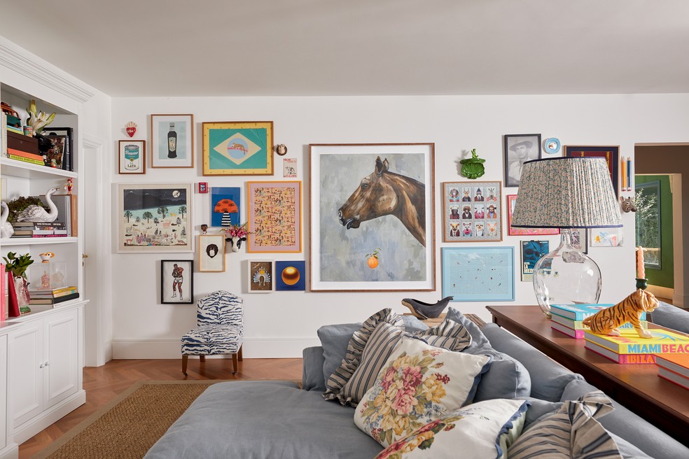 Outro ângulo do living com sofá, almofadas, abajur e cadeirinha, tudo da Entreposto, e, na parede, obras escolhidas por Laura e Chay, como o quadro de cavalo, do artista argentino Martin Lanezan — Foto: Deco Cury