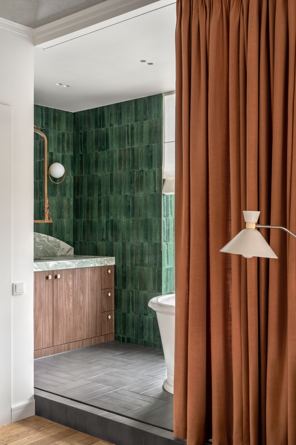 No banheiro, isolado pela cortina terracota, a designer de interiores combinou revestimentos verde esmeralda com acabamentos em dourado — Foto: Andrey Bezuglov