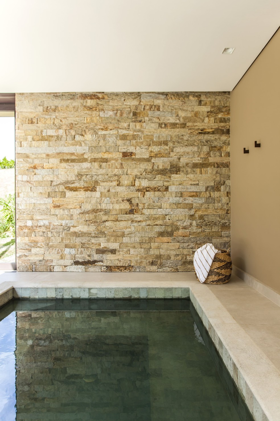 Assinado pelo escritório Korman Arquitetos, esse ambiente possui piscina revestida de pedras, além de sua borda e a parede principal — Foto: Eduardo Pozella