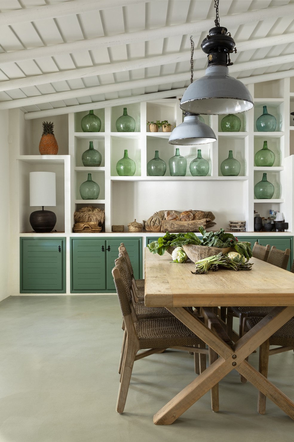 Conectada com a sala de jantar, parte da cozinha marca pela marcenaria com acabamento em verde e as garrafas artesanais do mesmo tom, produzidas no Algarve — Foto: José Manuel Ferrão