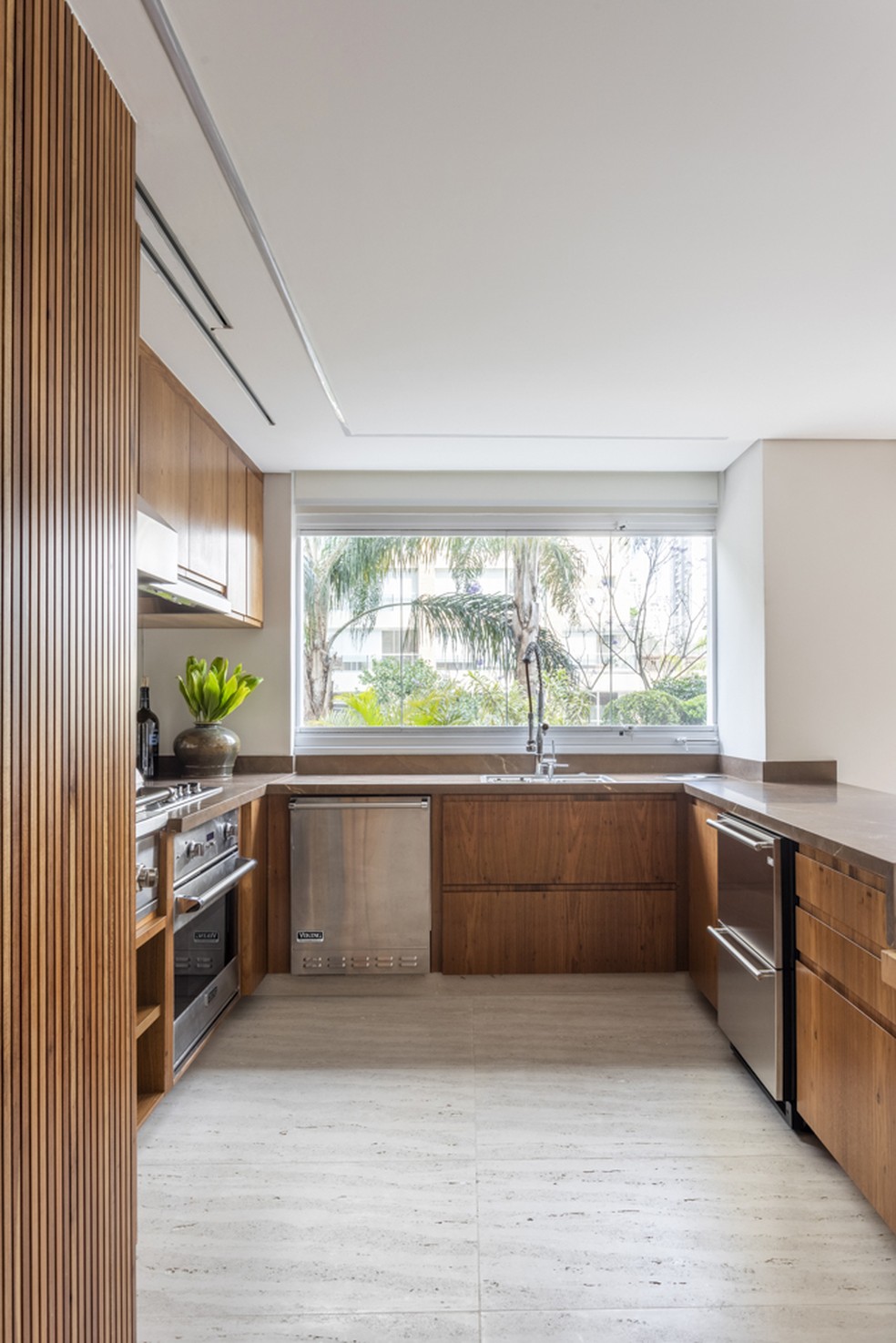 Na cozinha, armários planejados ocupam todo o perímetro e, no piso, a arquiteta optou por mármore travertino — Foto: Thiago Travesso