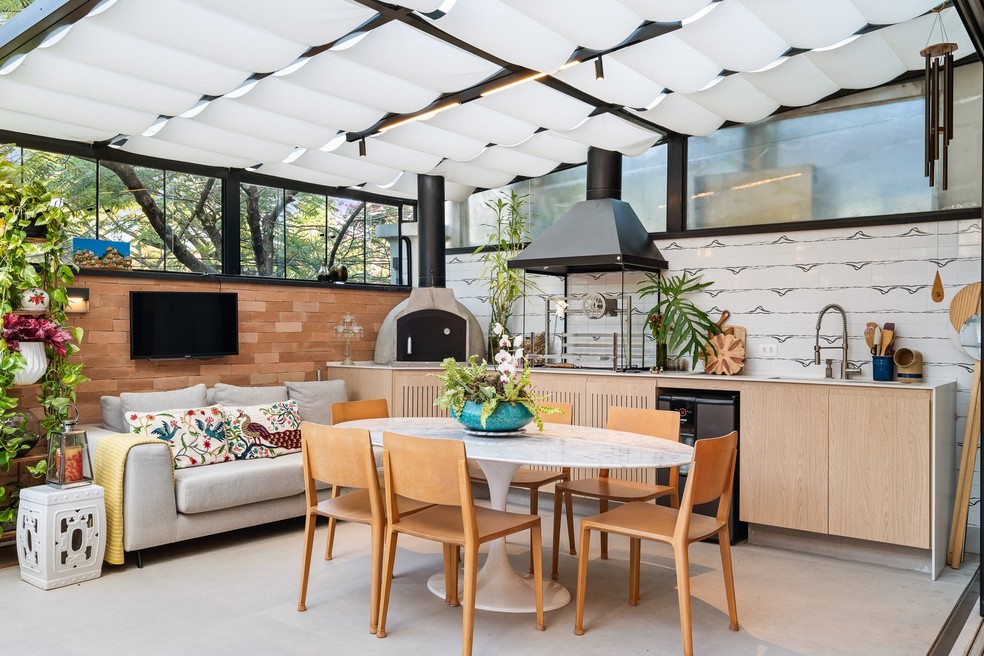 Espaço da churrasqueira com espaço para sofá, televisão e mesa de jantar — Foto: Flávio Dias