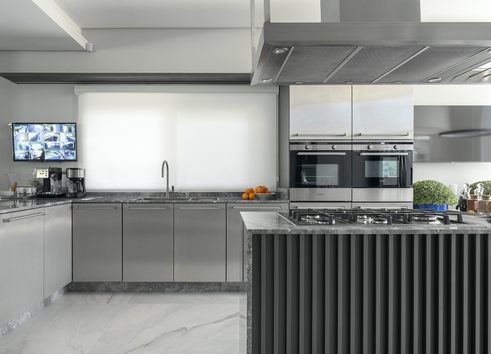 Integrada aos ambientes externos, a cozinha com tons de cinza é discreta e elegante — Foto: Lio Simas
