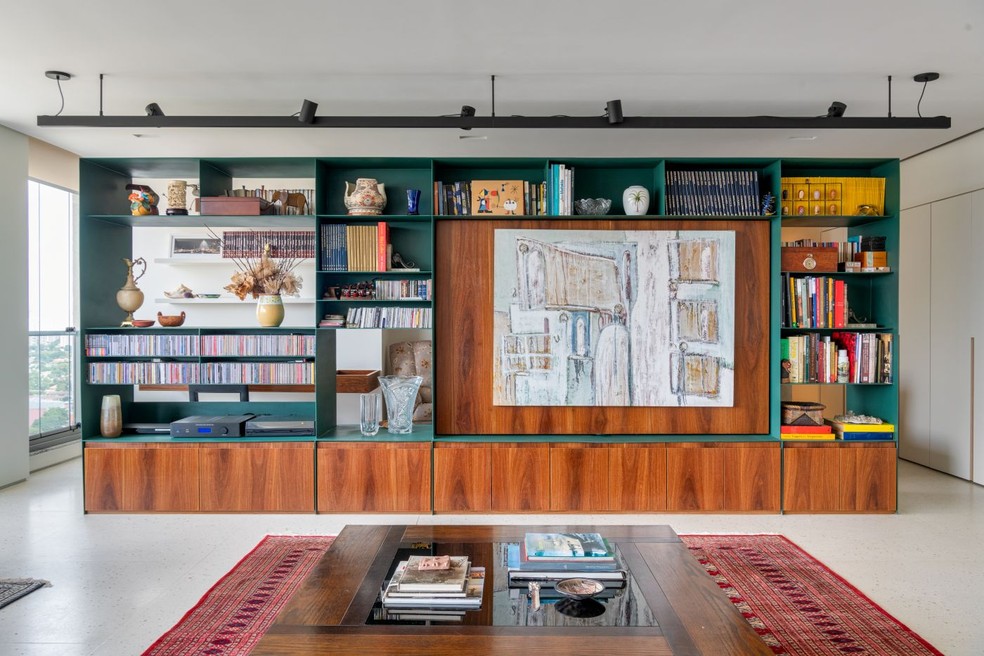 Nesta sala de estar, projetada pelo escritório COTA760 Arquitetura, a estante acomoda a coleção de livros dos moradores e peças afetivas — Foto: Divulgação