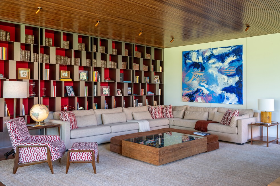 Na sala de TV, a estante vermelha com estrutura de aço abriga diversas coleções da família, junto à mesa de Etel Carmona, à poltrona da Dpot, à luminária da Herança Cultural e ao sofá do tapeceiro Christian Marchesini — Foto: Favaro Jr.