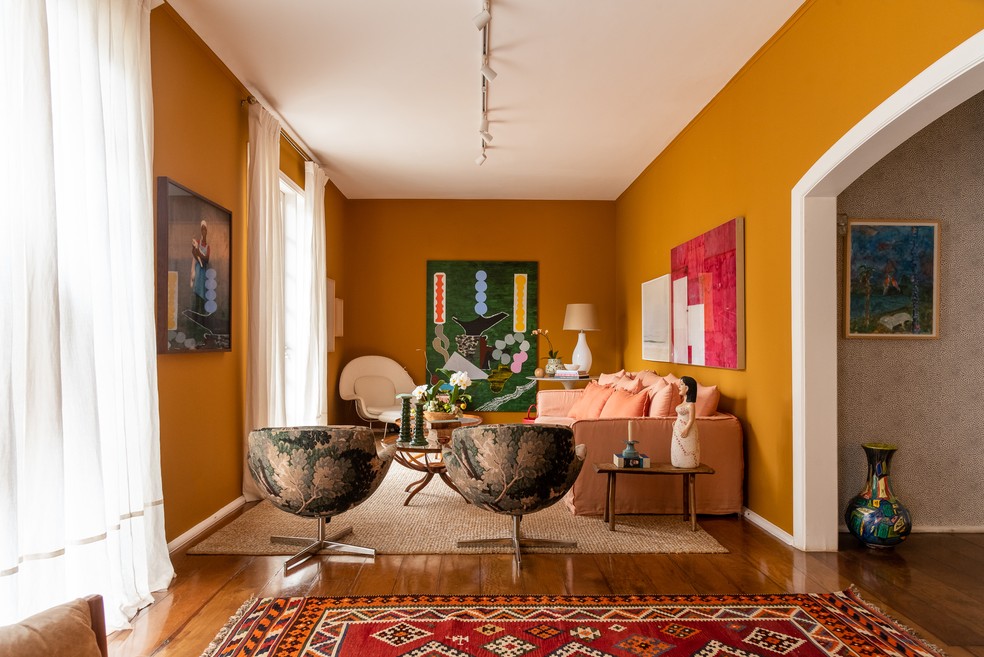 Sala de estar teve as paredes pintadas na cor caramelo e é cheia de cores - do sofá às telas penduradas — Foto: Wesley Diego Emes/Divulgação