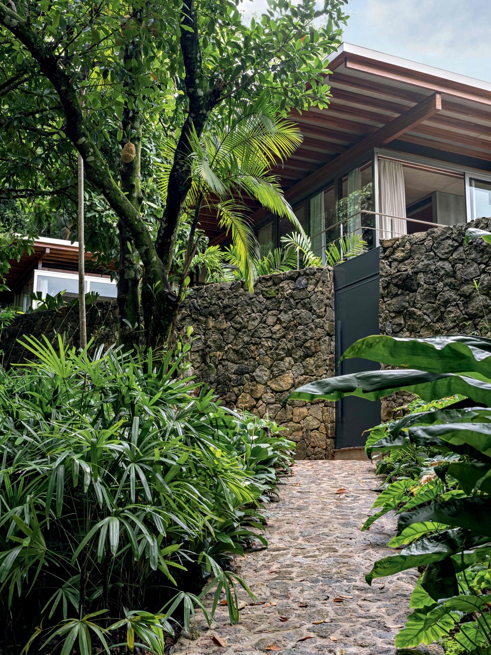 Reformada pelo escritório Andrade Morettin, esta casa conta com um lindo caminho de pedras até a porta da frente e é cercada pela natureza — Foto: Fran Parente