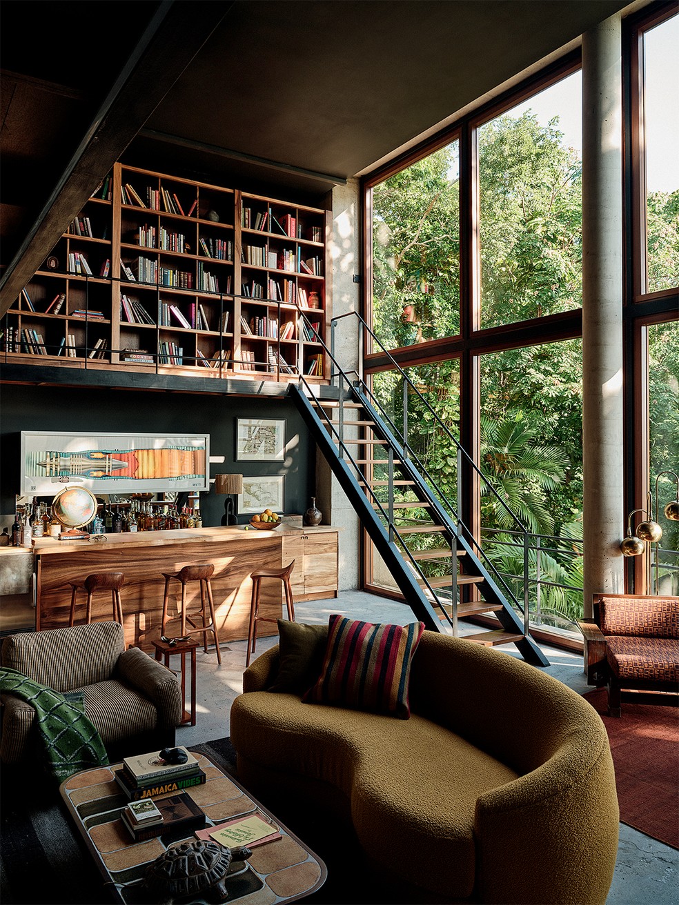 Na biblioteca, destaque para o sofá curvo Giselle, de Mitchell Gold + Bob Williams, revestido com tecido da Nobilis, e para a mesa de centro de Roger Capron – ao fundo, bar e estantes de madeira de guango jamaicano desenhados por Freecell Architecture e Gia Wolff — Foto: Frank Frances