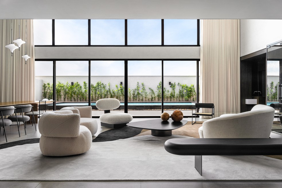 Com pé direito duplo, a sala de estar recebe muita luz natural por meio dos panos de vidro que revelam a área externa — Foto: Estúdio NY18