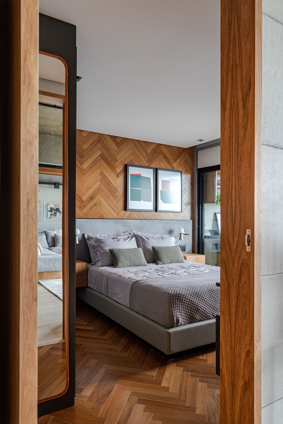 Em um dos quartos, o piso de madeira em padronagem espinha de peixe avança sobre a parede de cabeceira, propondo uma atmosfera bem aconchegante para o descanso — Foto: Gabriela Daltro