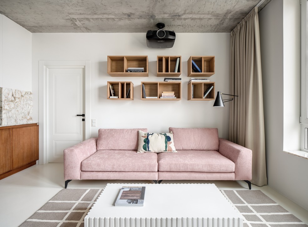 O sofá de veludo rosa é o protagonista da sala de estar, que ainda conta com nichos e um projetor  — Foto: Andrey Bezuglov