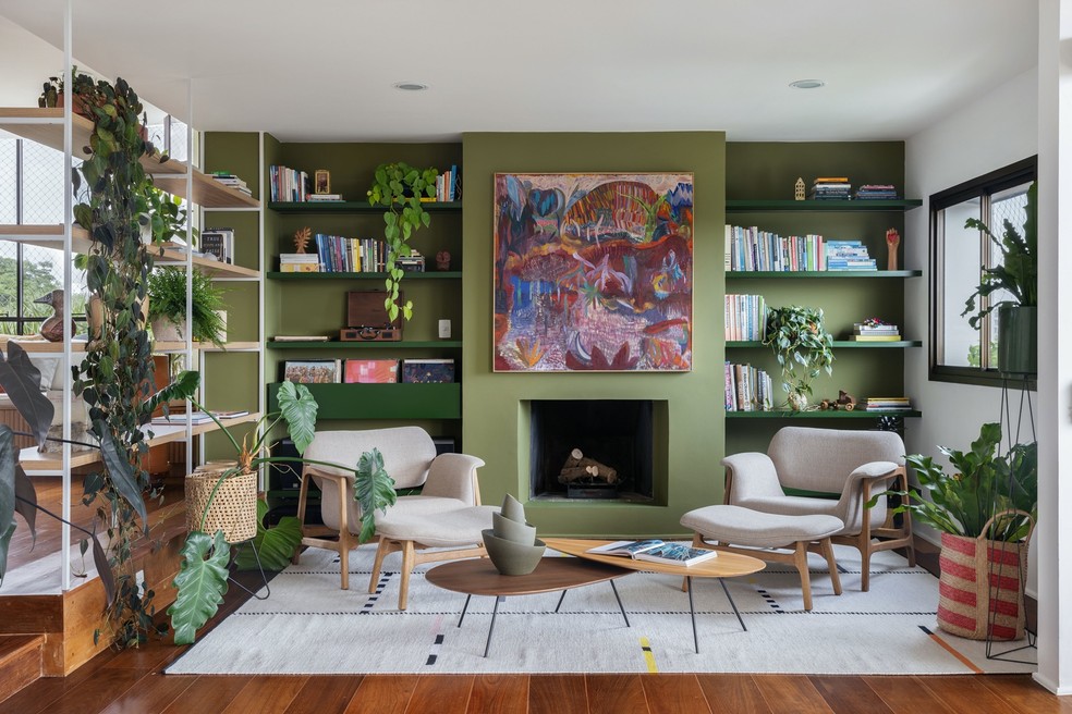 Nas paredes, prateleiras e plantas, a cor verde é protagonista na sala de estar — todo o piso de madeira desse ambiente é original do apartamento e foi restaurado — Foto: Maura Mello