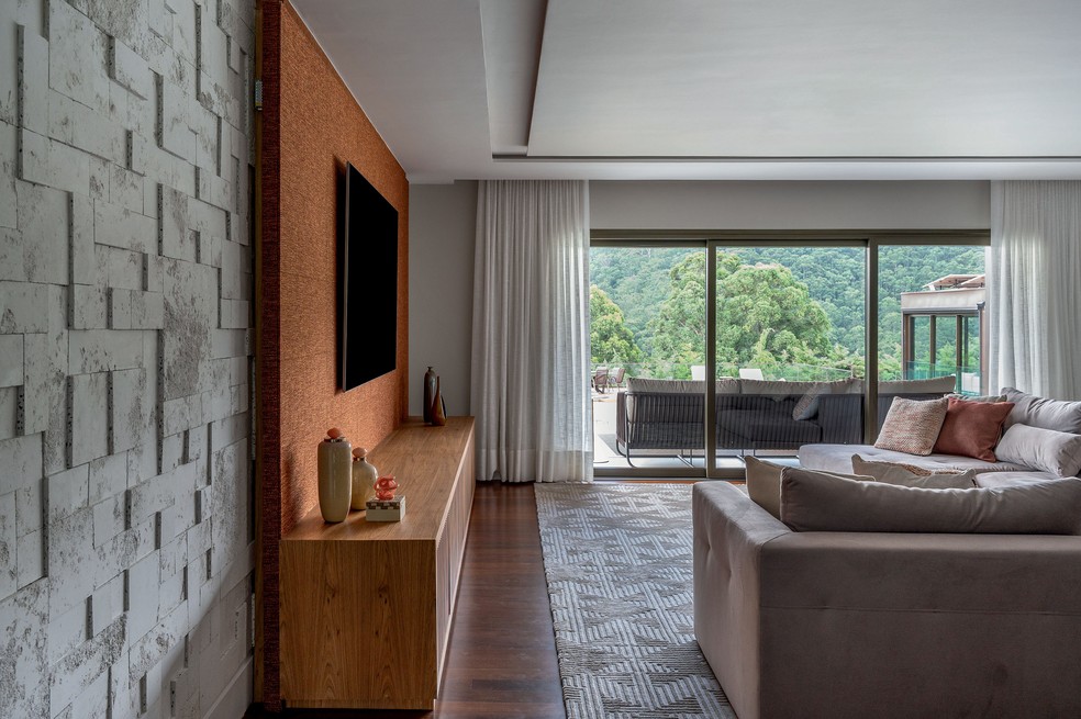 O living evidencia a variedade de texturas selecionadas pela arquiteta, com destaque para a parede revestida de material cimentício branco e os tapetes da By Kamy, com tramas e degradês delicados — Foto: Favaro Jr./divulgação