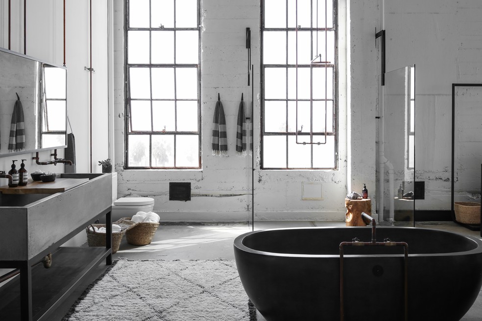 Banheiro traz pia em cimento queimado, assim como o piso, e banheira na mesma paleta — Foto: Alexander Design/Divulgação