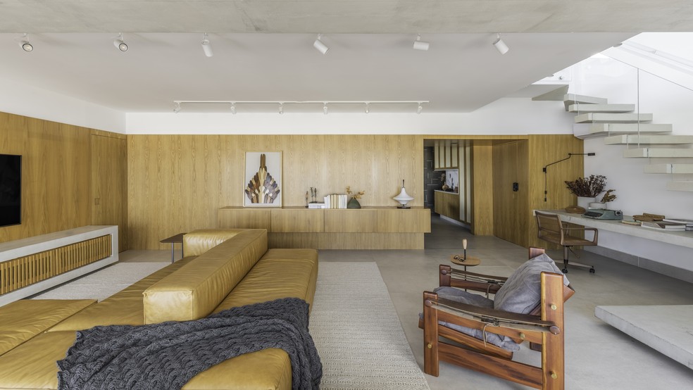 No living, o sofá mantem o mesmo tom da madeira carvalho, que compõem os painéis ao fundo — Foto: Guilherme Pucci