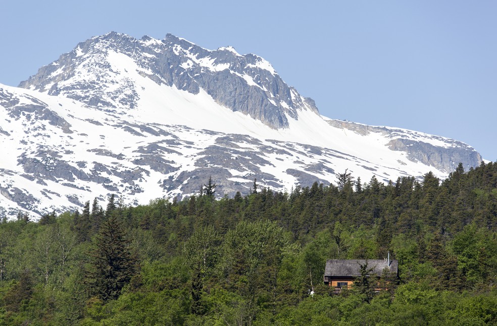 Esta casa está situada entre árvores perenes, ao pé de uma montanha, no Alasca, nos EUA — Foto: virsuziglis/GettyImages