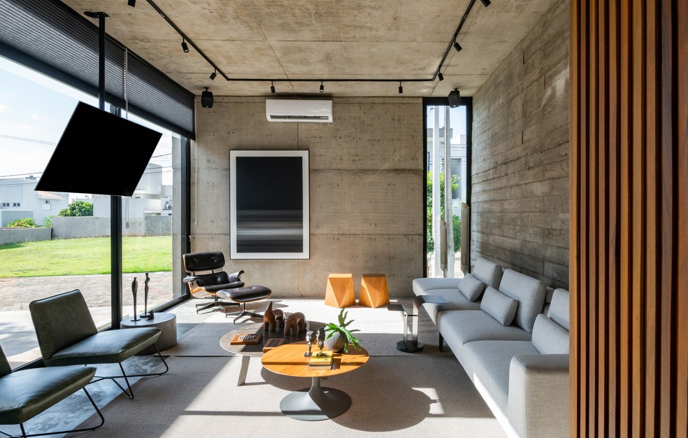 Sala de estar traz o uso do concreto como protagonista, nas paredes e no teto, junto aos móveis em tons neutros e com madeira na composição — Foto: Fávaro Junior