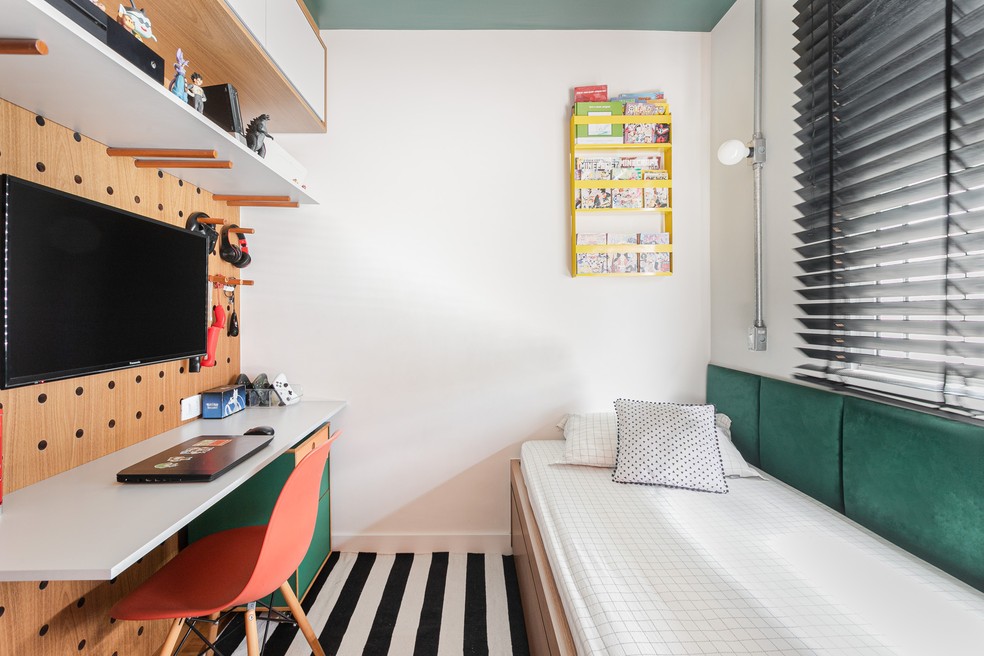 Em um dos quartos dos filhos, a cama foi posiciona abaixo da janela enquanto o painel de madeira abriga a TV e uma bancada de estudos — Foto: Gisele Rampazzo 